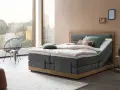Modernes Boxspringbett mit Holzrahmen und grauem Stoffbezug. Die Matratze wirkt etwas zu hart, aber die Kissen laden zum Entspannen ein.