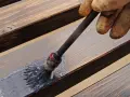 Mit einem Pinsel wird ausgeblichenes Holz aufgefrischt. Die graue Lasur verleiht den Dielen neuen Glanz.