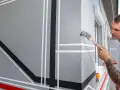 Mann streicht geometrische Muster auf eine graue Fassade. Die Temperatur nachts ist ideal für das Streichen.
