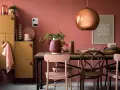 Ein Esszimmer mit altrosa Wänden. Ein kupferfarbener Lampenschirm und ein Holzmöbelstück mit gelben Türen. Welche Farbe zu altrosa? Zarte Rosatöne und Erdtöne passen gut.