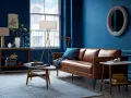 Gemütliches Wohnzimmer mit tiefblauen Wänden, brauner Ledercouch und einem hellblauen Teppich. Die Kombination aus Blau und Braun schafft eine warme Atmosphäre.