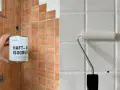 Vorbereitung zum Fliesenfärben: Eine Hand hält eine Dose Haftgrund, während ein Roller weiße Farbe auf Fliesen aufträgt.