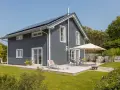 Modernes Haus mit dunkler Holzfassade, die zweifarbig gestrichen ist. Sonnige Terrasse mit Gartenmöbeln und Liegestuhl.