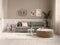 Ein Wohnzimmer mit salbeigrünem Sofa. Braune und cremefarbene Kissen, ein beiger Hocker und eine helle Wand zeigen, welche Farbe passt zu Salbei.
