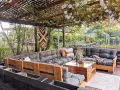 Gemütliche Paletten Lounge Ideen für den Garten. Ein großer Ecksofa aus Paletten mit grauen Polstern und Holztisch. Weinreben und Lichterketten überdachen den Sitzbereich.