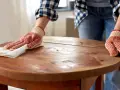 Person mit Handschuhen poliert einen alten Holztisch. Die Pflege des Holztisches ist wichtig, damit er lange schön bleibt.