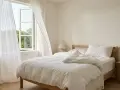 Ein helles Schlafzimmer mit offenem Fenster und weißen Vorhängen. Auf dem Nachttisch steht ein Thermometer, das die angenehme schlafzimmer temperatur anzeigt.