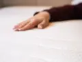 Eine Hand liegt auf einer weißen Matratze. Wann sollte man eine Matratze austauschen? Wenn sie durchgelegen ist oder Flecken hat.