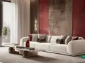 Luxuriöses Wohnzimmer mit einem cremefarbenen Sofa, das mit Kissen in verschiedenen Texturen und der Akzentfarbe bordeaux dekoriert ist. Die Wand hinter dem Sofa ist in einem tiefen Rotton gehalten.