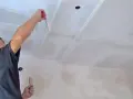 Mann trägt Grundierung auf Rigips-Decke auf.