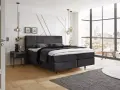 Ein modernes Schlafzimmer mit einem dunklen Boxspringbett ja oder nein? Helle Wände, Holzboden und ein Fenster mit Stadtblick.