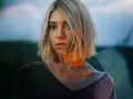 Blonde Frau mit Bob-Schnitt, deren Gesicht von warmem Licht beleuchtet wird, das sich mit dem blauen Abendhimmel mischt.