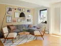 Gemütliches Wohnzimmer mit grauem Sofa, zwei Sesseln und vielen Bildern an der gelben Wand. Perfekt, um die Wand abzukleben und neu zu gestalten.