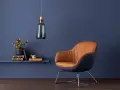 Ein Sessel mit braunem Leder und dunkelblauem Stoff vor einer blauen Wand. Orange Blumen auf einem Regal zeigen, welche Farbe passt zu Blau.