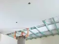 Mann verkleidet die Decke mit Gipskartonplatten. Die Unterkonstruktion ist sichtbar.
