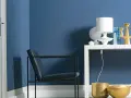 Ein Sessel vor einer Wand in moderner Wandfarbe. Auf einem Regal stehen eine Lampe, eine Vase und ein goldener Kerzenständer.