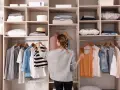 Frau sortiert Kleidung in einem offenen Schrank. Sie überlegt, was sie anziehen soll, um den offenen Schrank zu verkleiden.