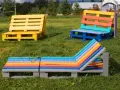 Bunte Palettenmöbel im Garten: Eine gelbe Bank, eine mehrfarbige Sitzbank und eine bunte Liege laden zum Entspannen ein. Paletten streichen ohne schleifen ist hier die Devise.