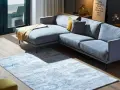 Ein moderner Wohnbereich mit einem grauen Ecksofa und einem Teppich, der richtig platziert unter dem Sofa liegt.