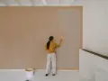 Frau streicht Wand mit neuer Farbe. Man fragt sich, wie lange braucht wandfarbe zum trocknen, während die alte Farbe noch sichtbar ist.