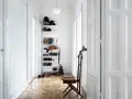 Schmaler Flur mit weißer Wandfarbe, Holzboden und einem Regal voller Schuhe und Hüte. Ein Stuhl steht bereit.