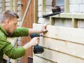 Mann renoviert Holzfassade, schraubt neue Bretter an. Werkzeug liegt bereit.
