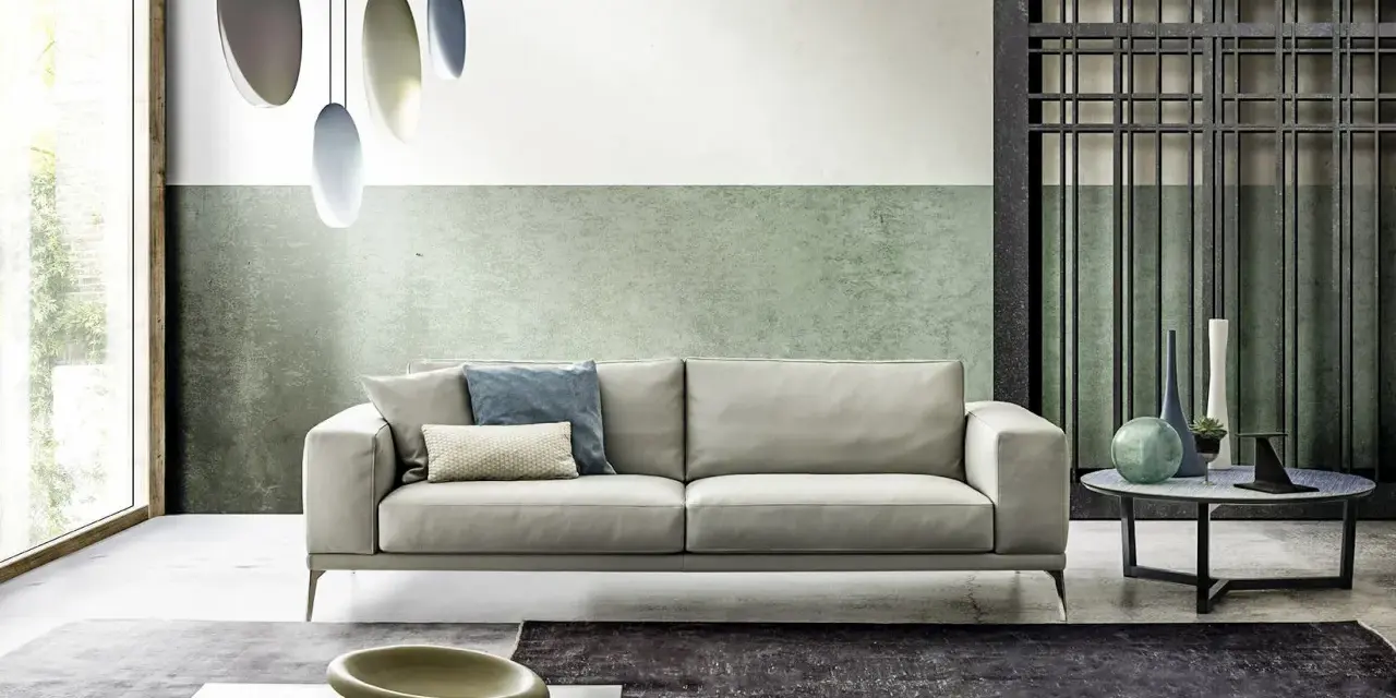 Modernes Wohnzimmer mit hellem Sofa, grüner Wand und stilvollem farbkonzept. Hängende Lampen und dekorative Vasen ergänzen das Ambiente.