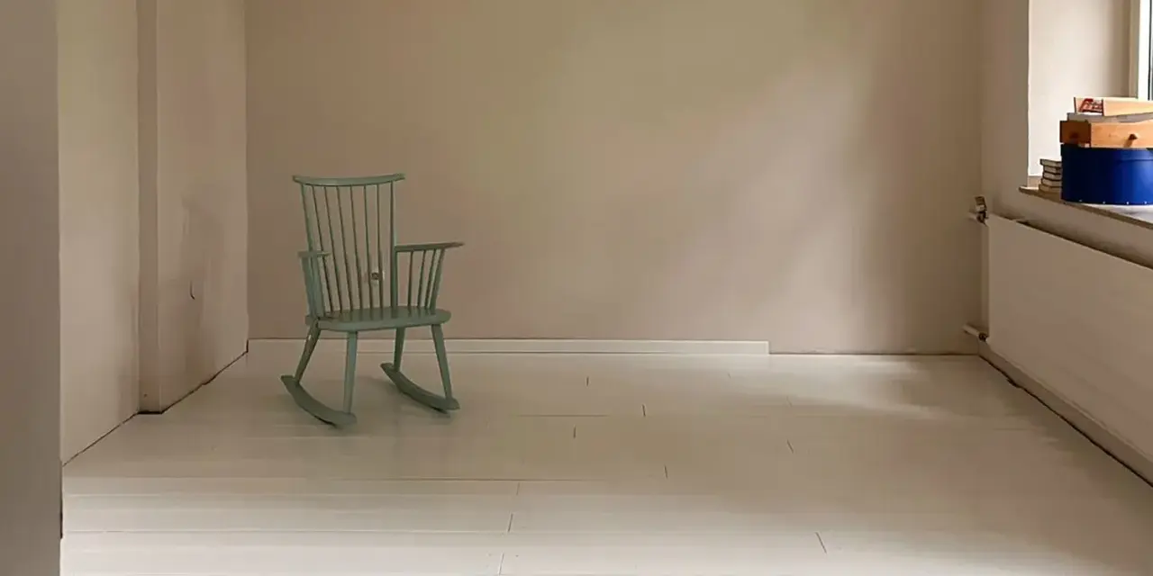 Ein hell gestrichener holzboden mit einer mintgrünen Schaukelstuhl.