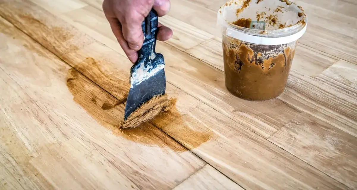 Mit einem Spachtel und Holzpaste werden Kratzer aus einem Holztisch entfernt.