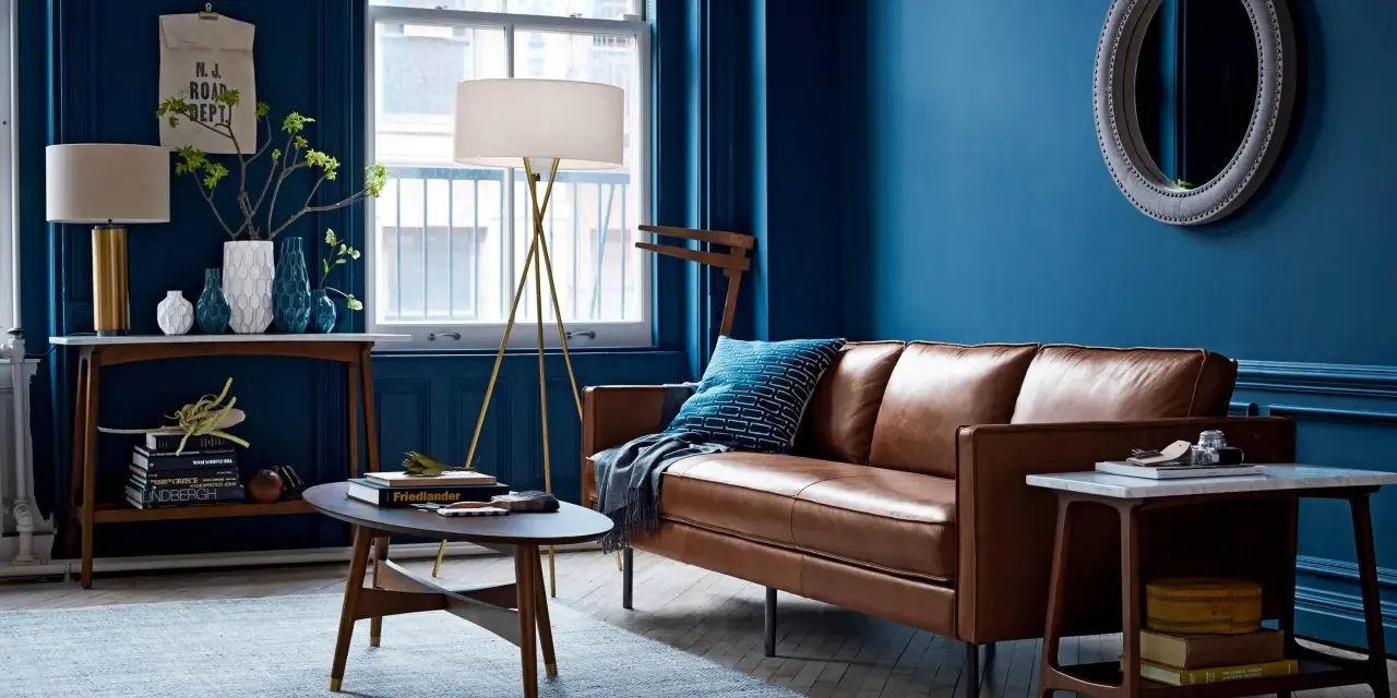 Gemütliches Wohnzimmer mit tiefblauen Wänden, brauner Ledercouch und einem hellblauen Teppich. Die Kombination aus Blau und Braun schafft eine warme Atmosphäre.