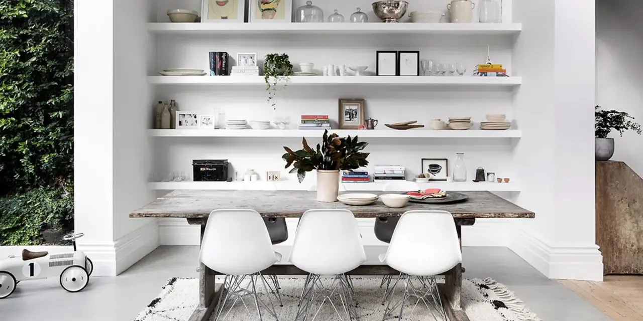 Moderne Esszimmer Wand Ideen: Weiße Regale voller Deko, Geschirr und Bilder über einem rustikalen Holztisch mit weißen Stühlen.