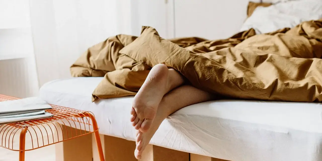 Füße ragen aus einem gemütlichen, braunen Bett hervor. Das Bett ist 210 cm lang und lädt zum Entspannen ein.