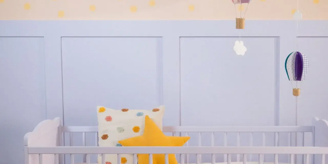 Ein frisch gestrichenes Kinderbett in zartem Lila, dekoriert mit bunten Kissen und schwebenden Heißluftballons.