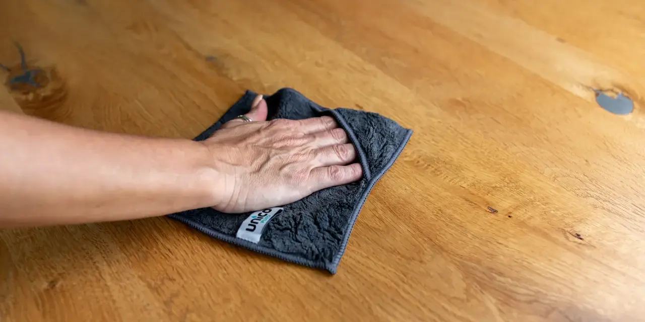 Hand wischt mit Tuch über Holzoberfläche, um schwarze Flecken zu entfernen. Hausmittel-Tipp für sauberes Holz.