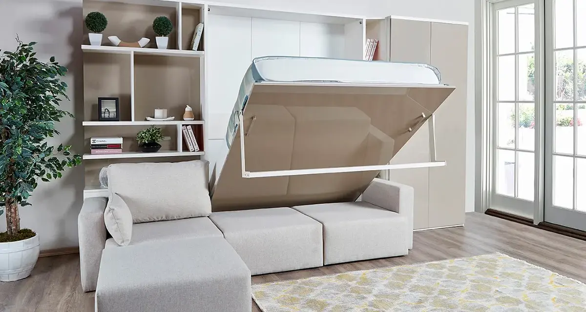 Ein verstecktes Bett im Wohnzimmer wird aus einem Schrank herausgeklappt. Daneben ein Sofa und ein Bücherregal.