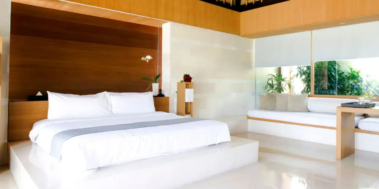 Luxuriöses Schlafzimmer mit einem großen weißen Bett, das den Unterschied zwischen einem King und Queen Bett verdeutlicht. Holzakzente und viel Licht.