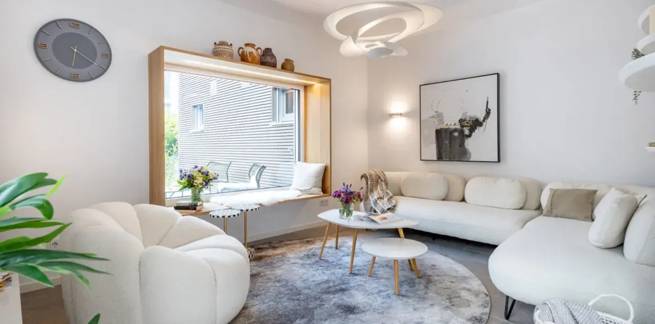 Modernes Wohnzimmer mit weißem Sofa, gemütlichem Sessel und einem Fensterplatz. Die schale dekorieren modern mit Vasen und Büchern.