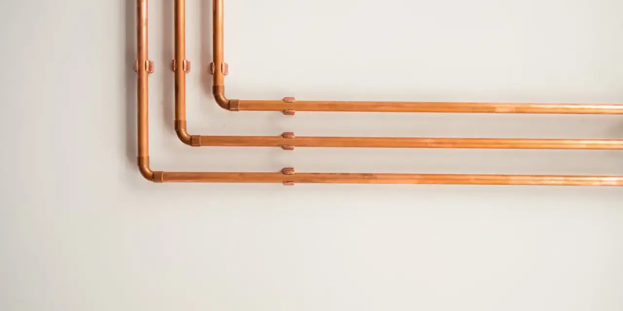 Kupferrohre an einer weißen Wand, die sich in einem rechten Winkel biegen. Tolle rohrverkleidung ideen für ein industrielles oder modernes Design.