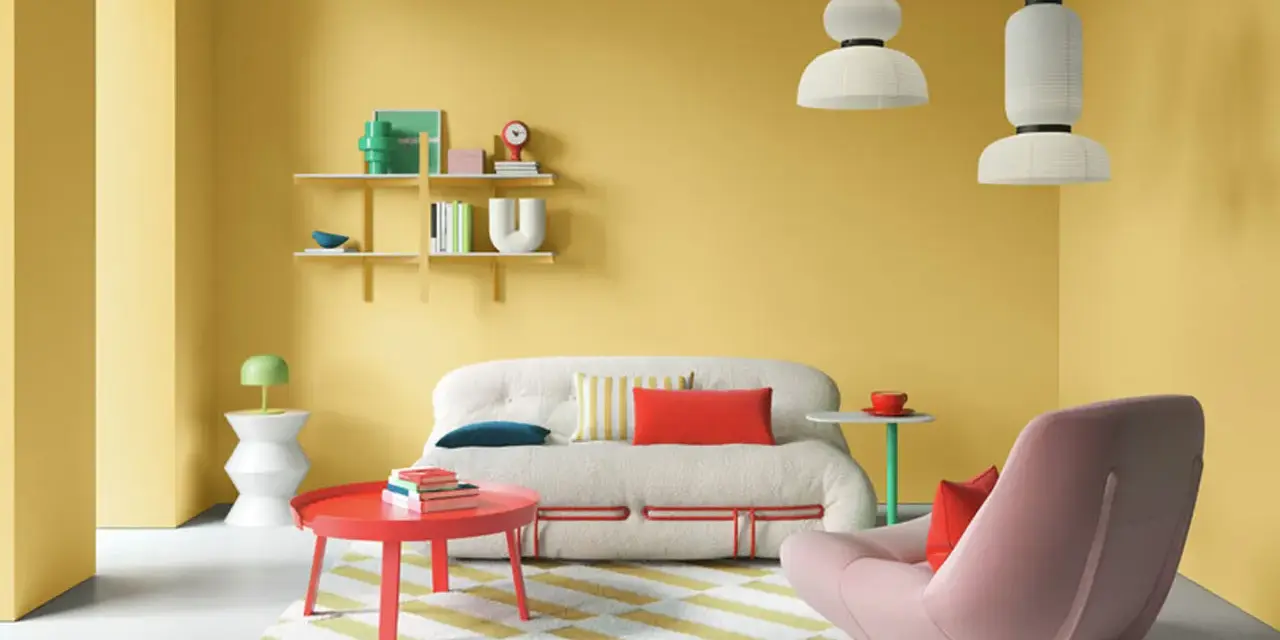 Ein Wohnzimmer mit gelben Wänden und einer auffälligen farb kombination aus Rot, Rosa und Weiß. Ein flauschiges Sofa und ein Sessel laden zum Entspannen ein.