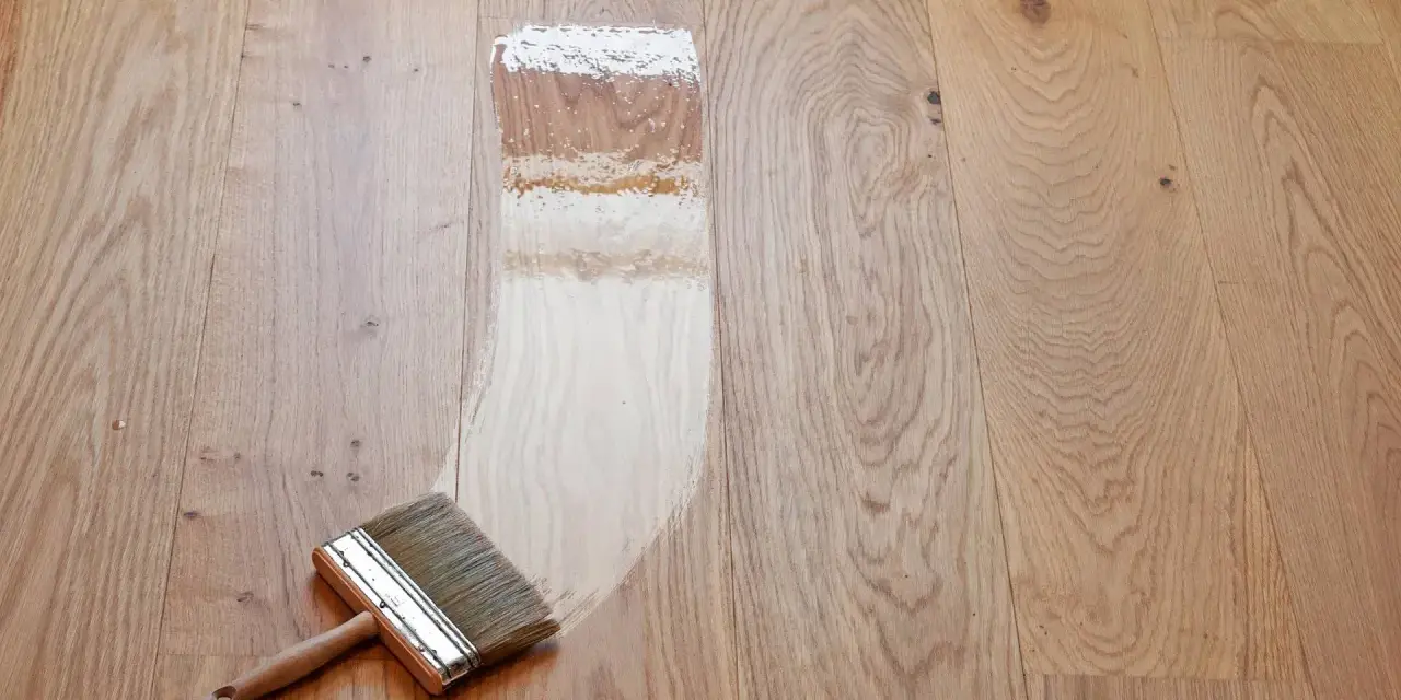 Breite Pinsel mit Holzgriff trägt Lack auf Parkett auf. Der Prozess, das Parkett zu versiegeln, zeigt den Unterschied zwischen unbehandeltem und frisch lackiertem Holz.