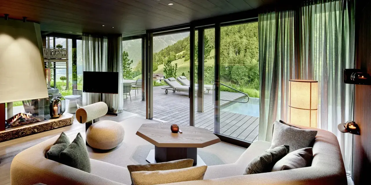 Gemütliches Wohnzimmer mit Kamin, großem Sofa und Bergblick. Die luxuriöse Chalet-Inneneinrichtung strahlt Wärme und Eleganz aus.