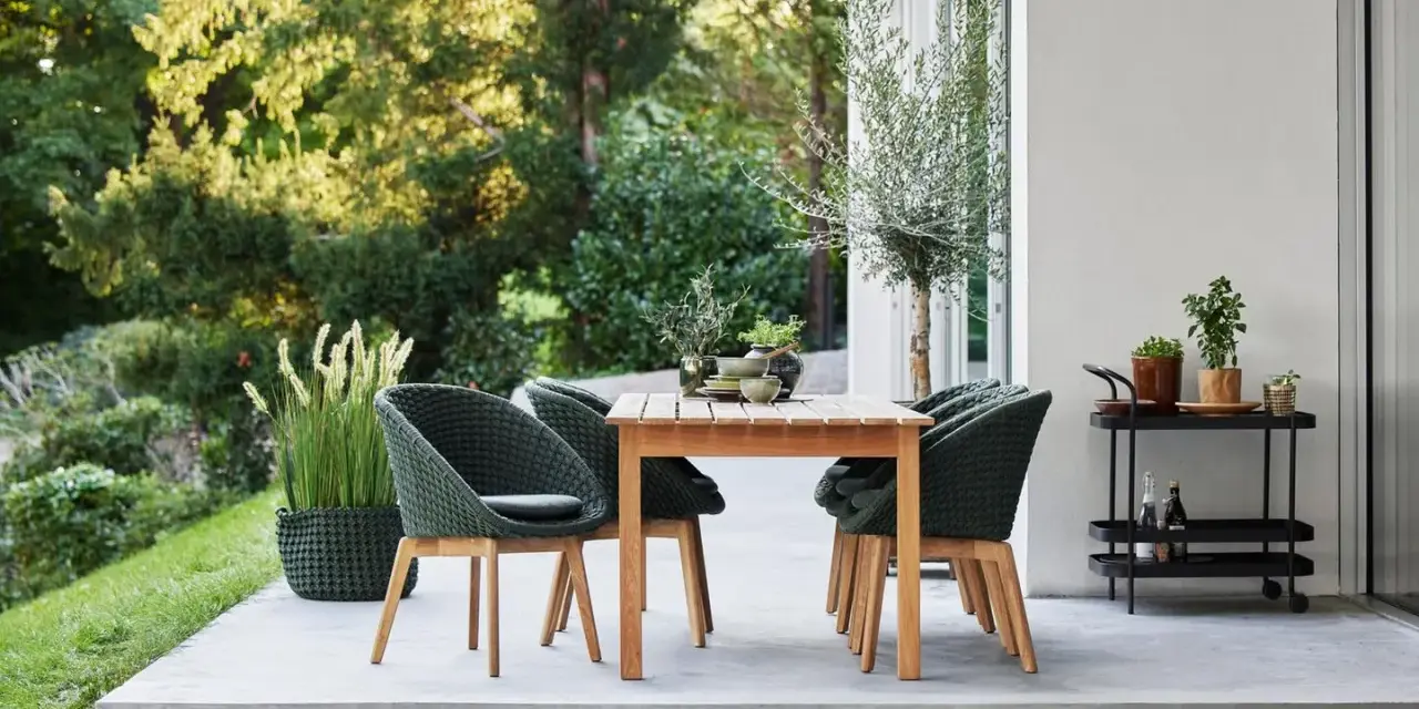Einladende Sitzgruppe auf einer modernen Terrasse, perfekt für die nächste terrasse renovieren. Grüne Korbsessel und Holztisch laden zum Verweilen ein.