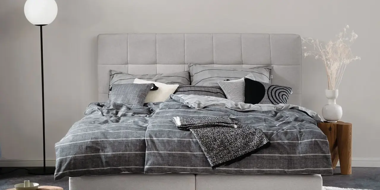 Stilvolle Schlafzimmer Ideen mit einem grauen Boxspringbett, gestreifter Bettwäsche und modernen Akzenten.