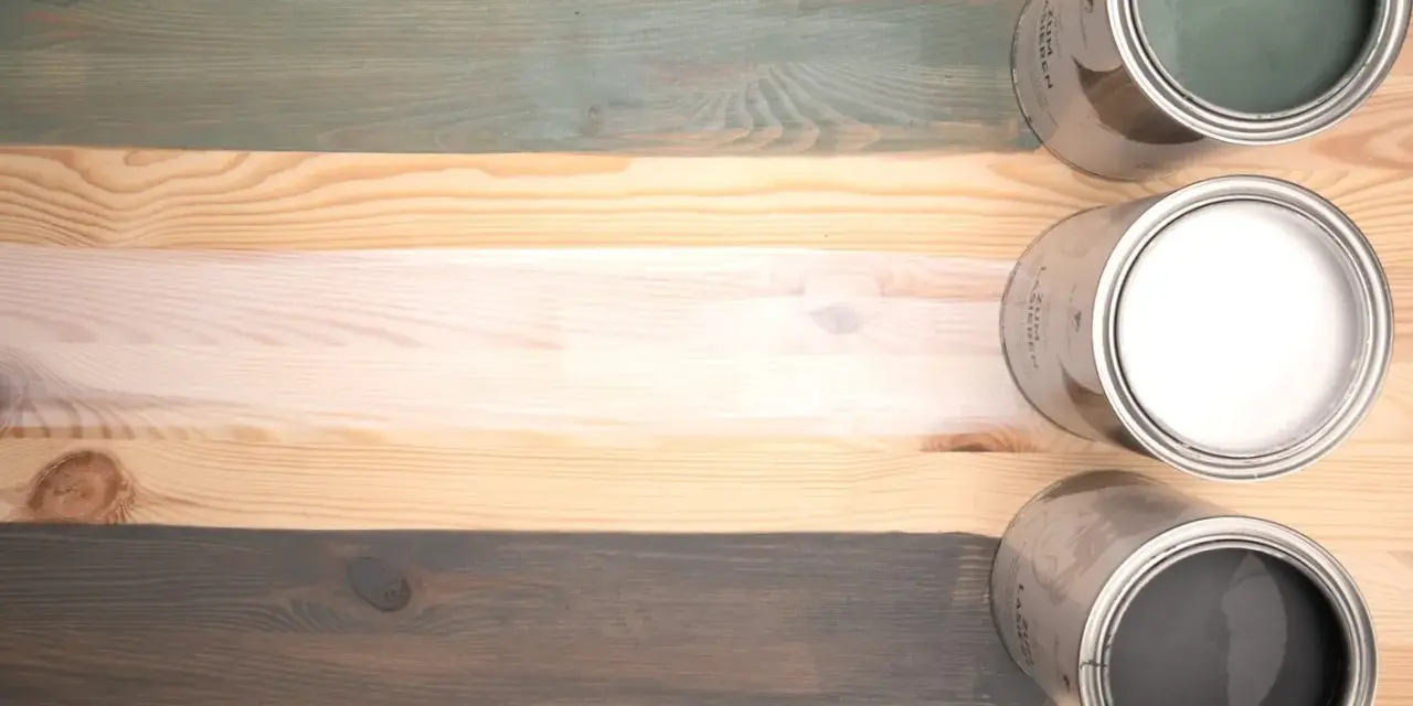 Holzlasur vorher nachher: drei Holzbretter mit unterschiedlichen Lasuren – grün, weiß und grau – und die passenden Dosen.