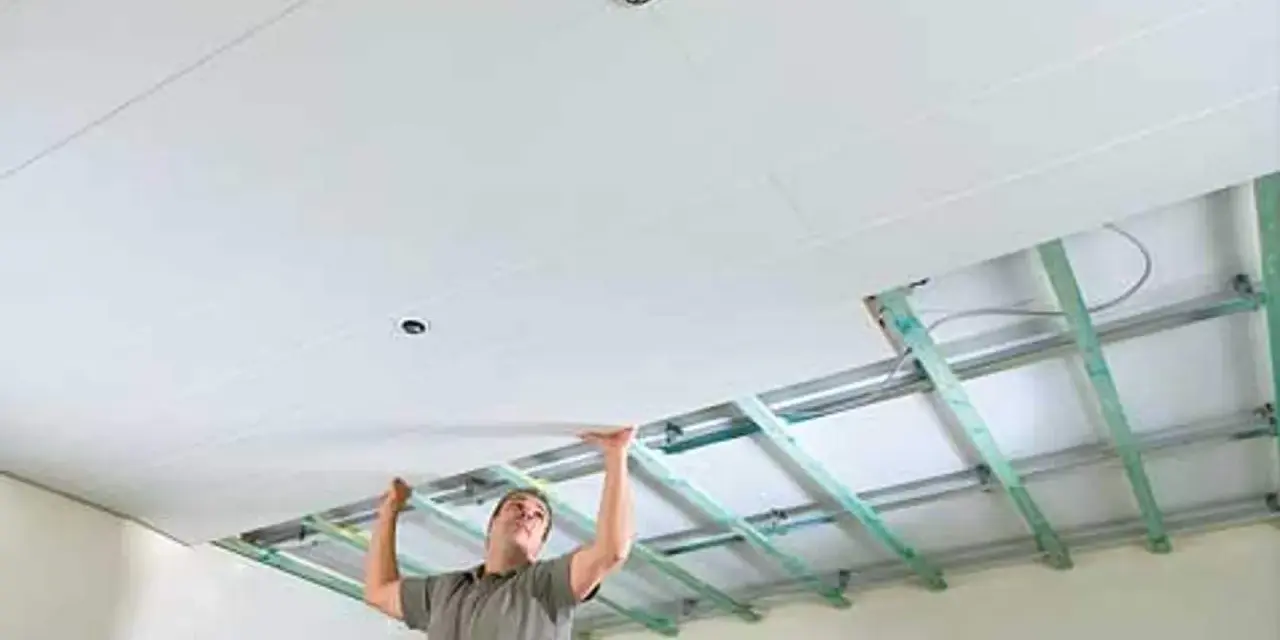Mann verkleidet die Decke mit Gipskartonplatten. Die Unterkonstruktion ist sichtbar.