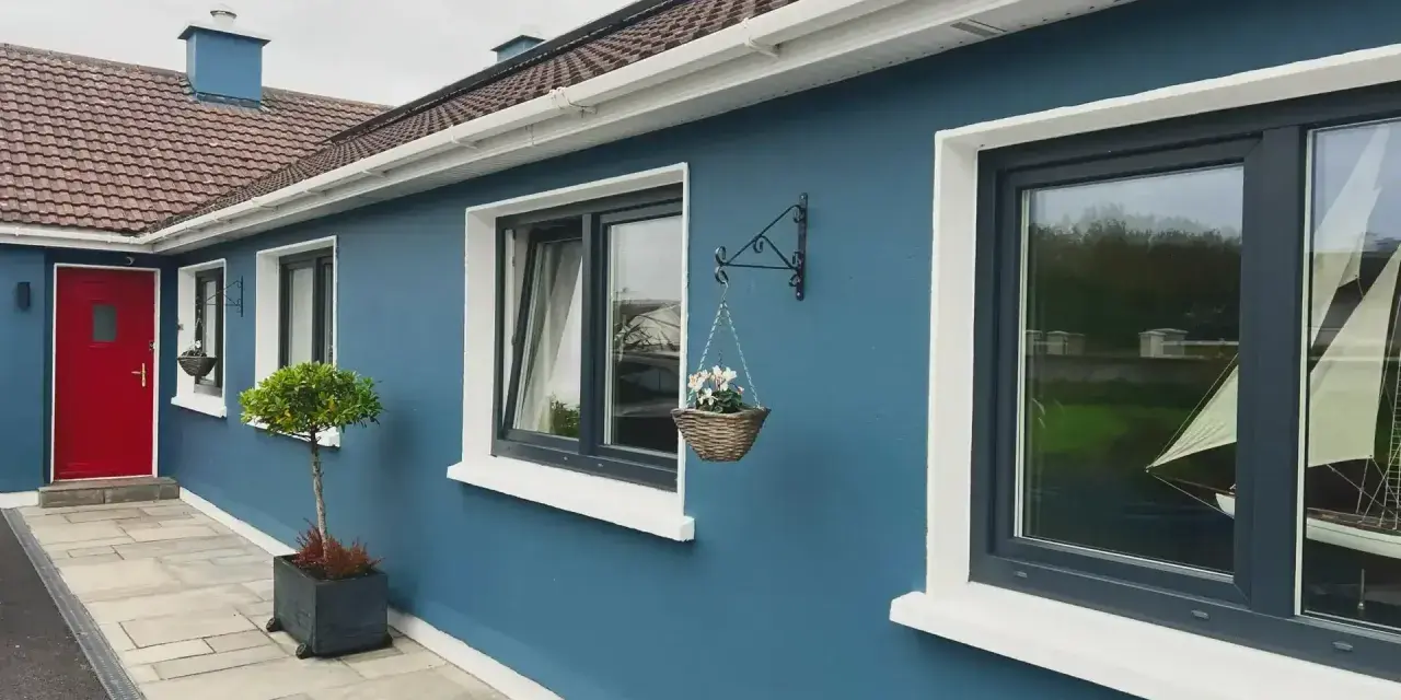 Ein blaues Haus mit roten Tür und dunklen Kunststofffenstern. Die Fensterrahmen sind in einem eleganten Anthrazit gehalten, was die modernen Kunststofffenster Farben unterstreicht.