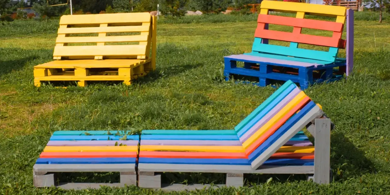 Bunte Palettenmöbel im Garten: Eine gelbe Bank, eine mehrfarbige Sitzbank und eine bunte Liege laden zum Entspannen ein. Paletten streichen ohne schleifen ist hier die Devise.