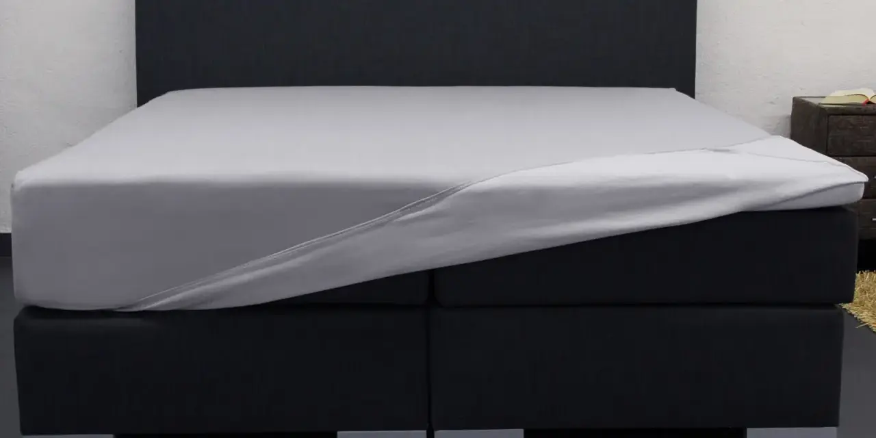 Ein graues Spannbettlaken wird über ein Boxspringbett gezogen. So beziehe ich ein Boxspringbett – einfach und schnell.