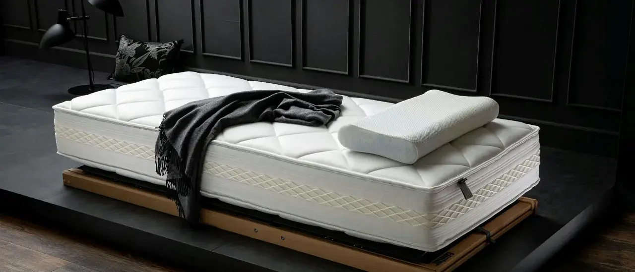 Eine neue, weiße Matratze mit Kissen und Decke liegt auf einem Holzrahmen. Zeit für einen Matratzenwechsel für erholsamen Schlaf.