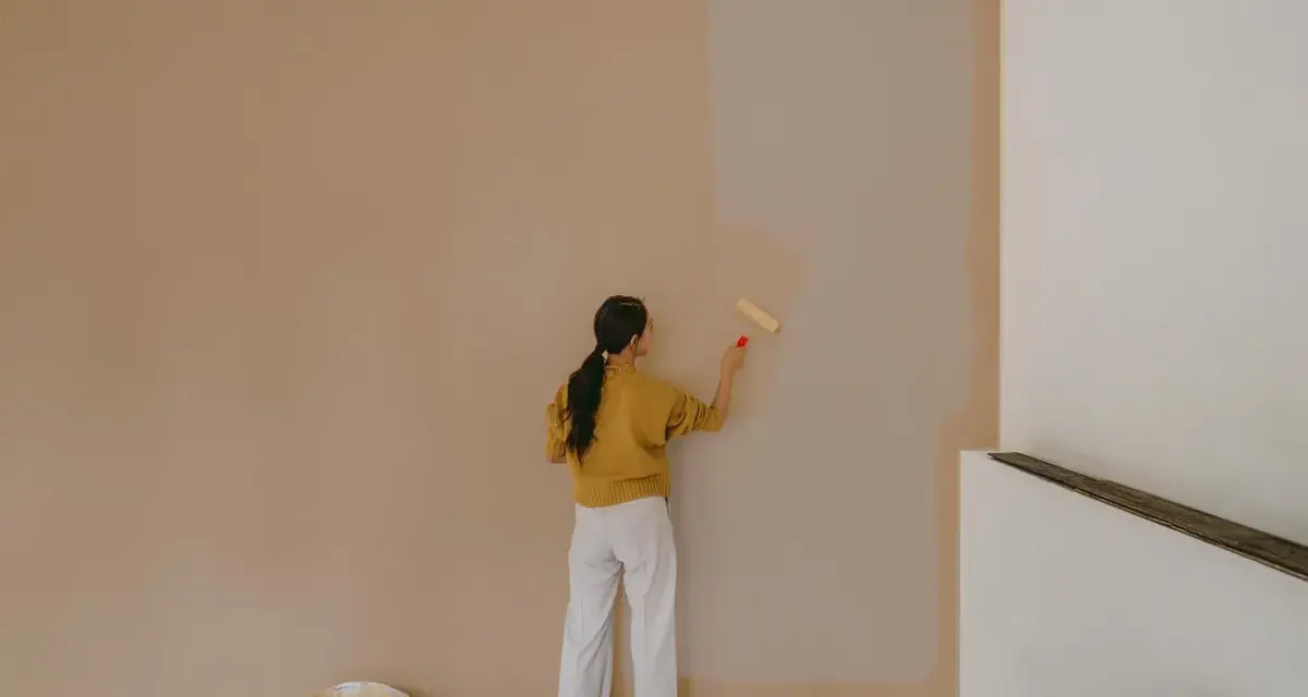 Frau streicht Wand mit neuer Farbe. Man fragt sich, wie lange braucht wandfarbe zum trocknen, während die alte Farbe noch sichtbar ist.